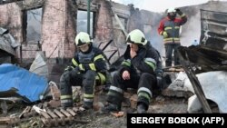Ukrainian firefighters rest after extinguishing a blaze in the suburbs of Kharkiv following a Russian drone attack. 