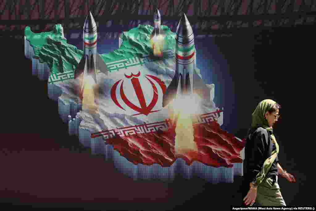 An Iranian woman walks past an anti-Israel banner with a picture of Iranian missiles on a street in Tehran.