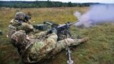 Two soldiers fire an M-249 light machine gun at an unknown location.