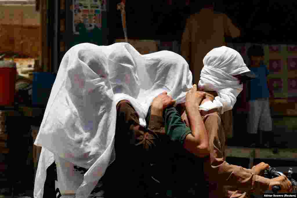 Men cover their heads with a wet cloth as they ride a bike in Jacobabad.