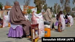 Afghan women sit after receiving food aid distributed by a charity foundation in Kandahar on March 28.