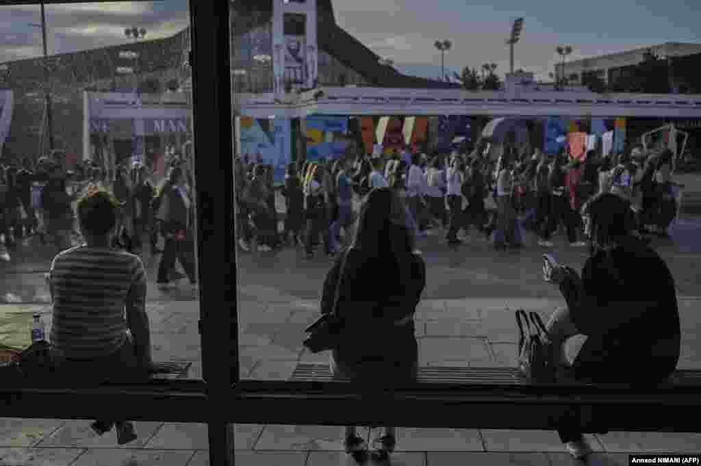 Žene na autobusnoj stanici promatraju prosvjed u Prištini 15. aprila. Prosvjednici su zatražili donošenje strožih mjera za počinitelje rodno uvjetovanog nasilja nakon ubojstva 21-godišnjakinje.