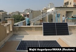 چند شهروند ایرانی در حال نصب پنل‌های انرژی خورشیدی بر پشت‌بامی در تهران در پاییز ۱۳۹۹/ چیزی حدود یک درصد از تولید برق ایران متکی بر انرژی‌های تجدیدپذیر است.
