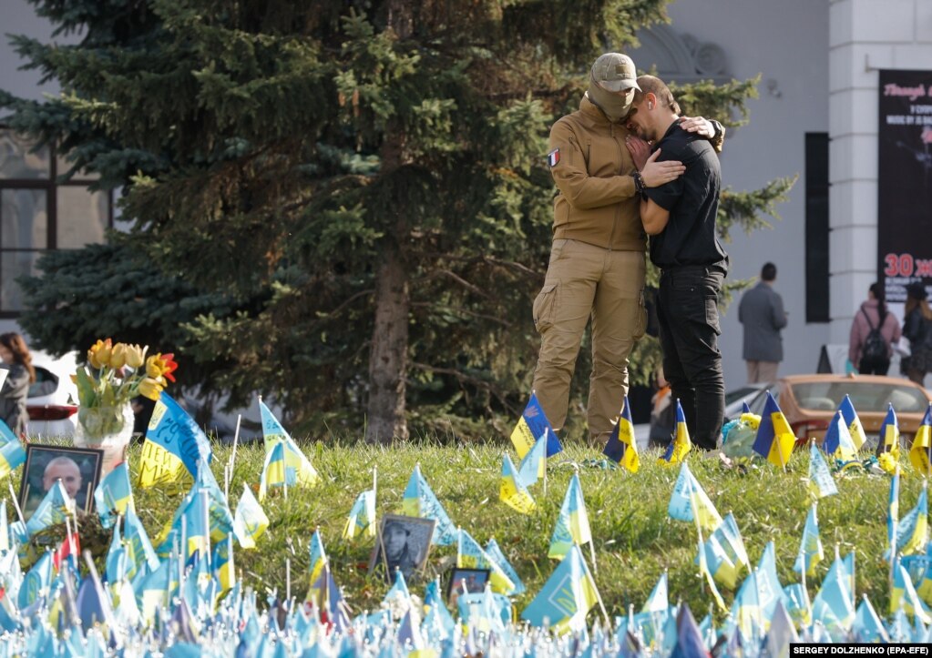 Dy burra përqafohen pranë flamujve të vendosur në Sheshin e Pavarësisë në përkujtim të ushtarëve të rënë ukrainas në qendër të Kievit, 30 tetor 2023.