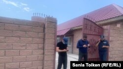 Сотрудник полиции и люди в штатском перед воротами дома Марата Жыланбаева. 23 мая 2023 года 