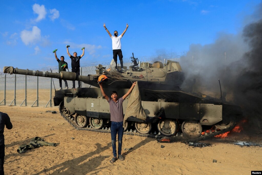 I palestinesi festeggiano mentre un veicolo militare israeliano brucia dopo essere stato colpito da uomini armati palestinesi che si sono infiltrati nelle aree del sud di Israele.