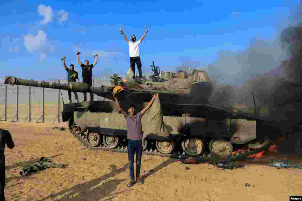 Palestinienii sărbătoresc în timp ce un vehicul militar israelian arde după ce a fost lovit de oameni înarmați palestinieni care s-au infiltrat în zonele din sudul Israelului.