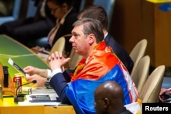 Președintele sârb Aleksandar Vucici poartă pe spate, sfidător, un steag sârb în timpul votului rezoluției din plenul ONU. New York, 23 mai.