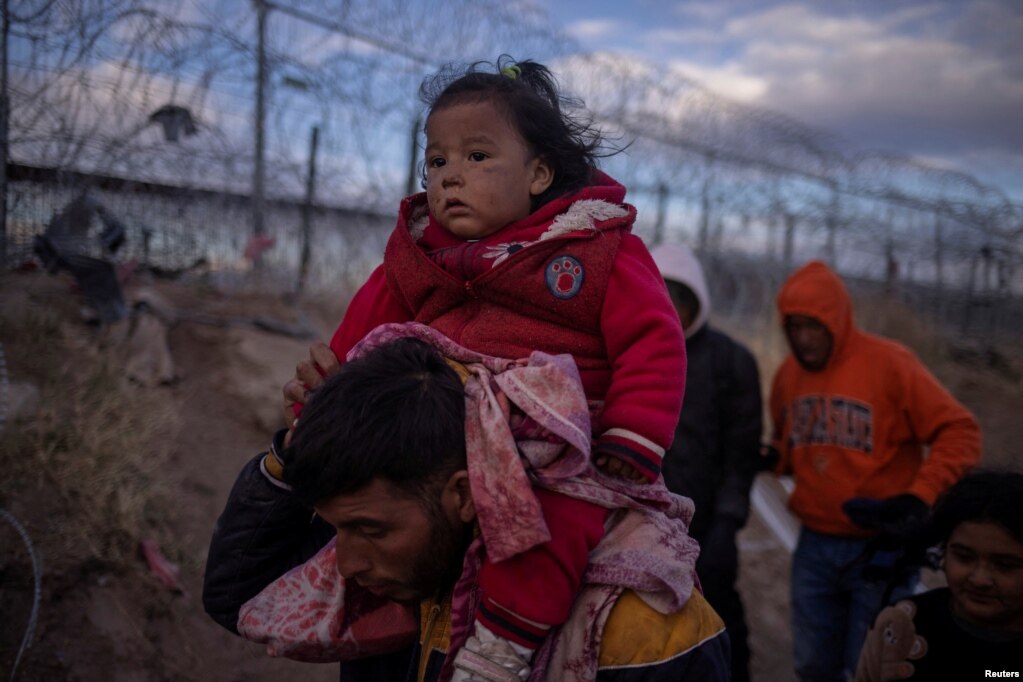 Jordan, një emigrant nga Peruja bart mbi qafë vajzën e tij njëvjeçare, Briana, teksa ata kërkojnë një pikë hyrjeje në Shtetet e Bashkuara, duke kaluar një gardh të mbushur telash me gjemba përgjatë bregut të lumit Rio Grande në El Paso. Teksas, SHBA, 26 mars 2024.