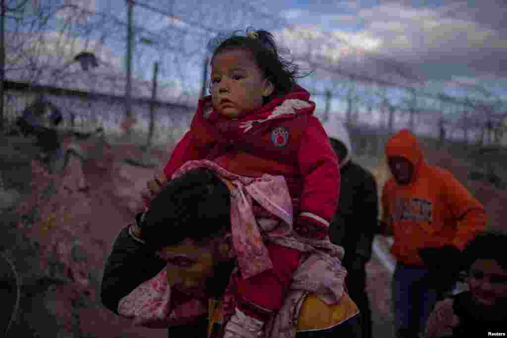 Jordan, një emigrant nga Peruja bart mbi qafë vajzën e tij njëvjeçare, Briana, teksa ata kërkojnë një pikë hyrjeje në Shtetet e Bashkuara, duke kaluar një gardh të mbushur telash me gjemba përgjatë bregut të lumit Rio Grande në El Paso. Teksas, SHBA, 26 mars 2024.