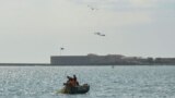 Рыбаки на лодке «Путина» в Севастопольской бухте, в небе над ними два российских ударных вертолета. Архивное фото