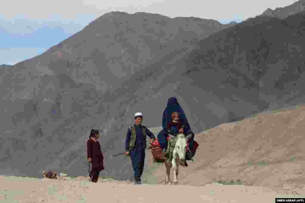 A burqa-clad woman and a child ride a donkey as two children walk along a road in Afghanistan&#39;s Badakhshan Province.