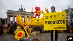 Экоактивист позирует с плакатом возле макета динозавра перед Бранденбургскими воротами во время митинга, посвящённого закрытию атомной станции в Берлине, Германия. 15 апреля 2023 года