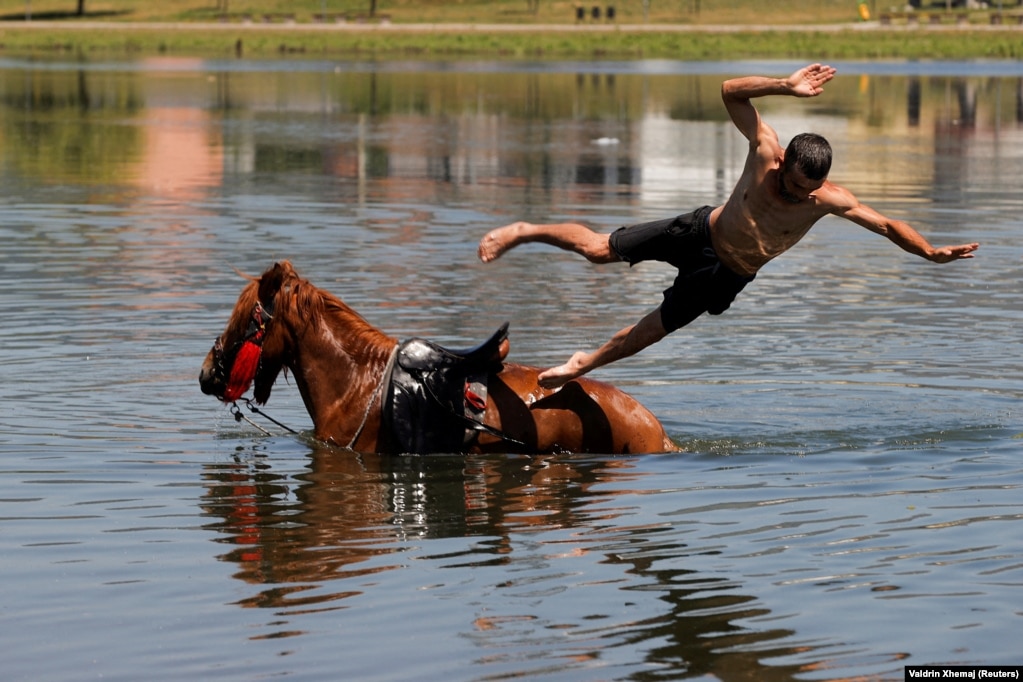 Një burrë hidhet nga një kalë me të cilin është futur në lumin Ibër për t&#39;u freskuar nga moti i nxehtë, Mitrovicë, Kosovë, qershor 2024.&nbsp;