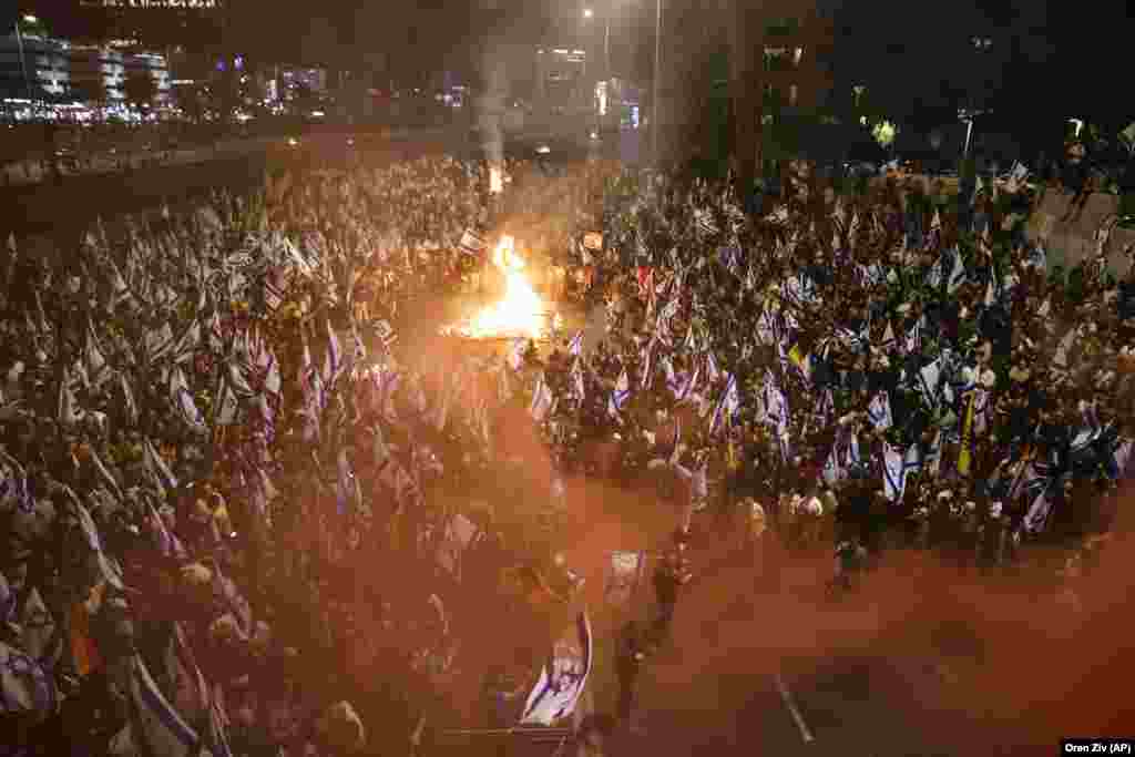 Protestuesit me flamuj në duar shihen përreth një zjarri në Tel Aviv.&nbsp; &nbsp;