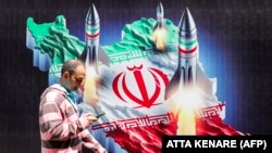 A man walks past a banner depicting missiles launching from a representation of the map of Iran colored with the Iranian flag in central Tehran.