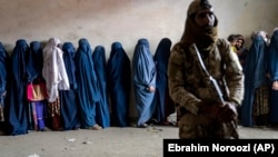 Taliban păzind femeile care așteaptă să primească rațiile alimentare distribuite de un grup de ajutor umanitar în Kabul, pe 23 mai.