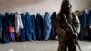 A Taliban fighter stands guard as women wait to receive food rations distributed by a humanitarian aid group in Kabul on May 23.