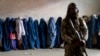 A Taliban fighter stands guard as women wait to receive food rations distributed by a humanitarian aid group in Kabul.