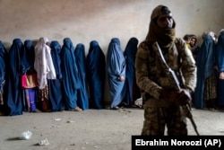 Un luptător taliban stă de pază în timp ce femeile așteaptă să primească rații de mâncare la Kabul în luna mai.