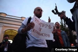 Arsenii Vesnin ține o coală de hârtie pe care scrie „Jos mâinile de pe jurnaliști” la un protest din Sankt Petersburg înainte de a părăsi Rusia.