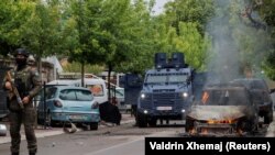 Pripadnici specijalne policije stoje pored zapaljenog automobila, nakon sukoba policije i grupe građana iz srpske zajednice, koji su pokušali da spreče novoizabranog gradonačelnika da uđe u kancelariju, u Zvečanu 26. maja 2023.