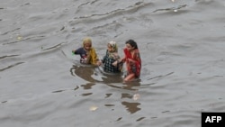 په لاهور کې تر باران وروسته پر سړک اوبه ډنډ شوې دي او درې ماشومانې په اوبو کې روانې دي - د اګست لومړۍ انځور.