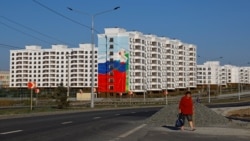 Женщина идет мимо недавно построенных домов в Мариуполе. Местные жители говорят, что новое жилье преимущественно отдают под ипотеку приезжим россиянам