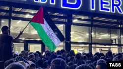Житель Дагестана размахивает палестинским флагом с надписью «Дагестан рядом с вами» во время пропалестинского митинга в аэропорту Махачкалы после прибытия регулярного рейса из Тель-Авива. 9 октября 2023 года