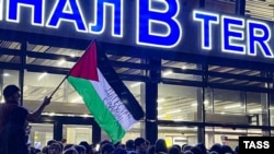 Një burrë e valëvit një flamur palestinez me mesazhin "Dagestani është me ju" gjatë një tubimi pro-palestinez në aeroportin e Makaçkalës, pas mbërritjes së një aeroplani nga Tel Avivi më 29 tetor, 2023.