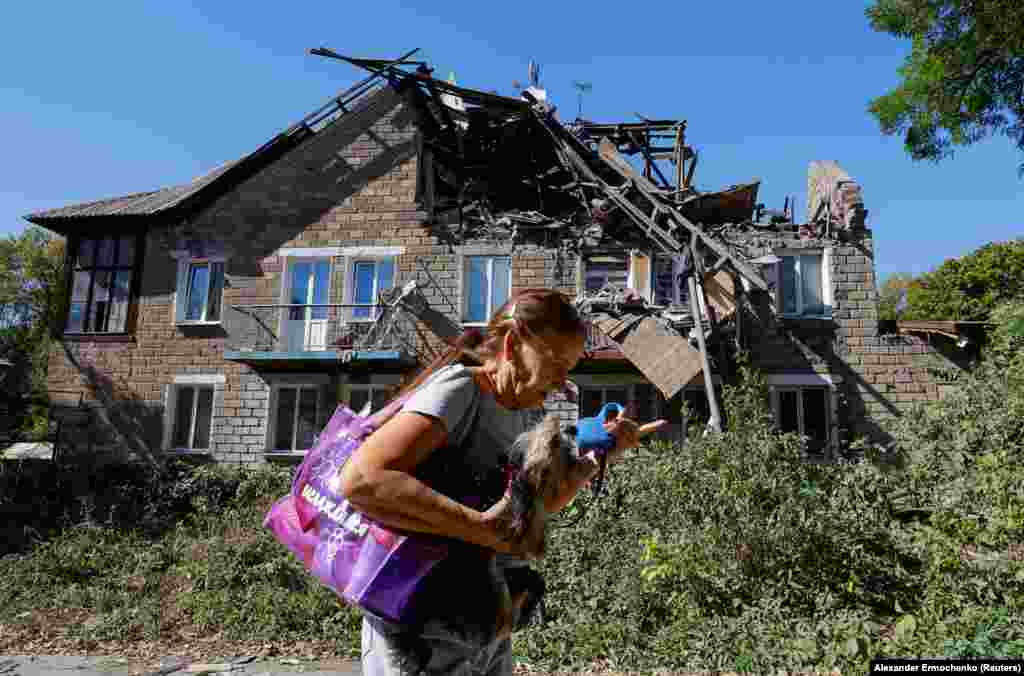 Një grua duke mbajtur një qen derisa kalon pranë një shtëpie të dëmtuar rëndë nga bombardimet e fundit në Donjeckun e kontrolluar nga Rusia.