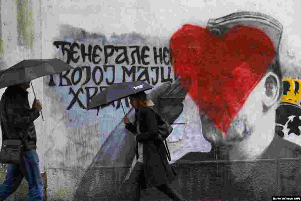 People walk by a mural of former Bosnian Serb military chief Ratko Mladic vandalized with red paint in Belgrade.