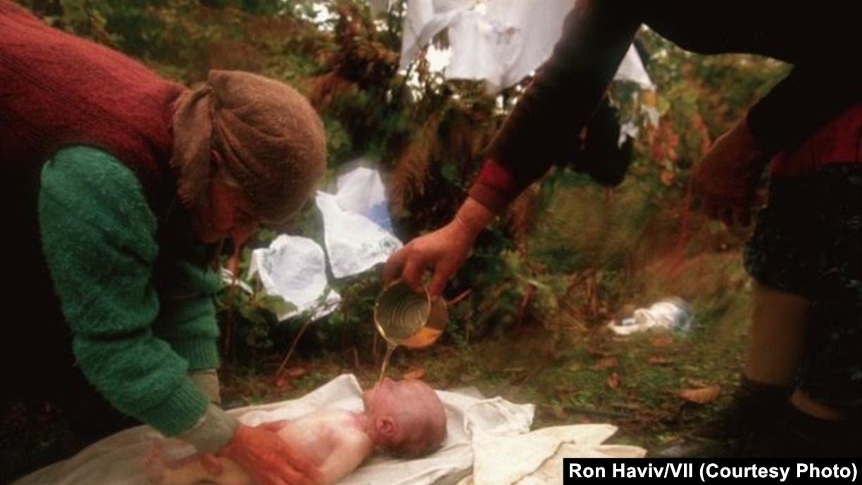 Shqiptarë të Kosovës, që ikën nga shtëpitë e tyre, në Drenicë, duke larë xhenazen e një foshnjeje pesëjavëshe, që vdiq nga kushtet e papërshtatshme në malet e Kosovës, në vjeshtën e vitit 1998, para varrimit të saj.