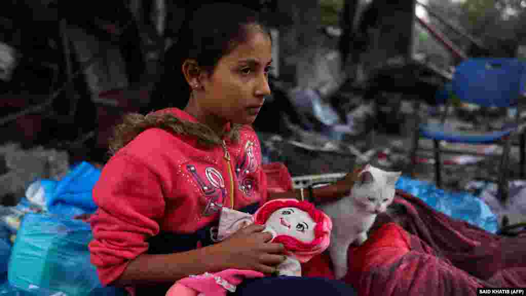 Egy palesztin lány a macskájával és a babájával az izraeli csapások által okozott pusztítás után összegyűjtött holmik mellett Kúzában, a Gázai övezet déli részén 2023. november 27-én, a tűzszünet idején