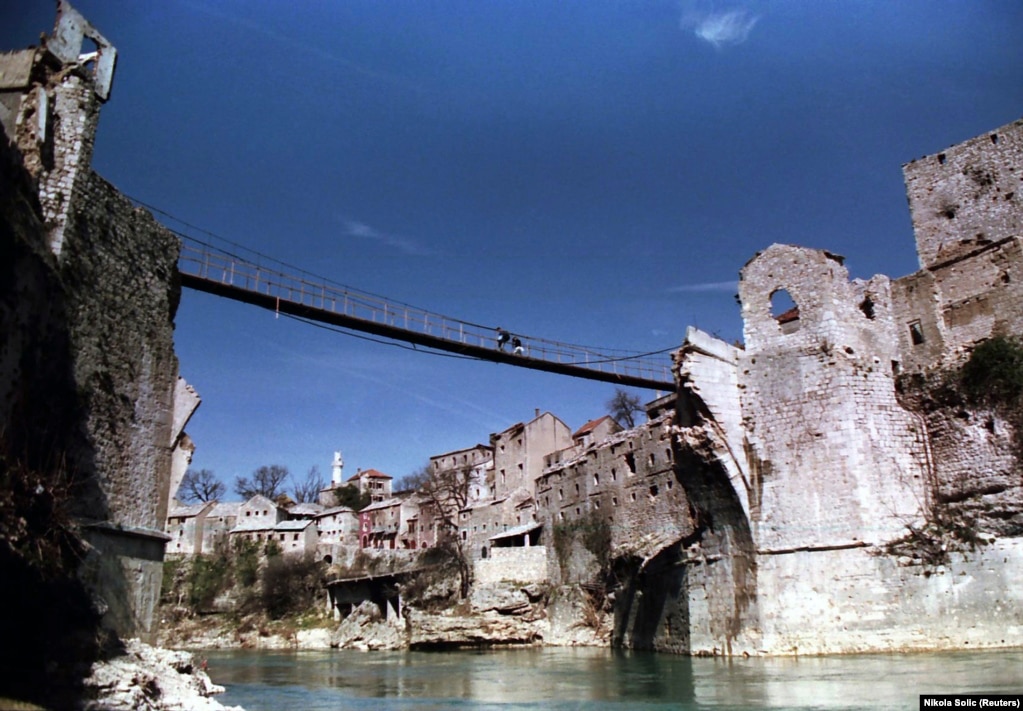 Banorët duke ecur nëpër një urë të përkohshme këmbësorësh mbi lumin Neretva, në mars të vitit 1994. Në vitet e pasluftës, në vend të urës së vjetër të shkatërruar u ngritën ura të ndryshme këmbësore që shqetësonin nervat. 