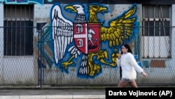 O tânără trece pe lângă o pictură murală pe un perete care prezintă o combinație dintre stema sârbă (stânga) și cea rusă, în Belgrad, Serbia. Imagine de arhivă.