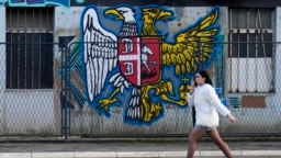 Egy lány sétál egy belgrádi falfestmény mellett, amelynek bal oldali része a szerb, jobb oldali része pedig az orosz címert ábrázolja