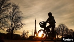 Një grua me biçikletë kalon, teksa në prapavijë shihet Kulla Eiffel. 22 nëntor 2023. 