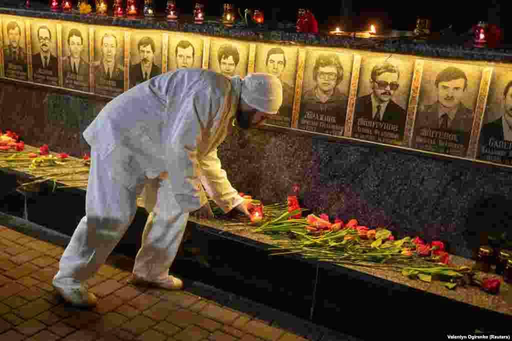 A csernobili erőmű egyik dolgozója gyertyát gyújt az atomkatasztrófában elhunyt tűzoltók és munkások emlékművénél az ukrajnai Szlavuticsban