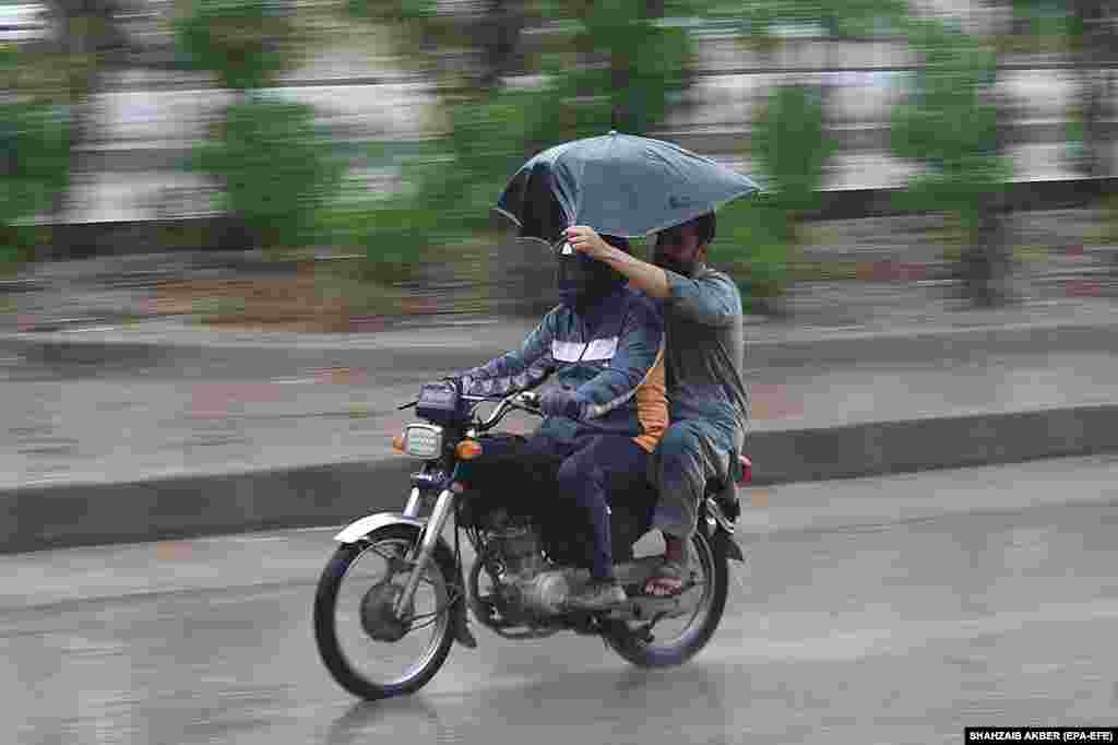 Two Pakistani men ride a motorbike during a heavy downpour in Karachi.