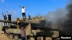 Снимка от 7 октомври от журналиста на свободна практика Ясер Кудих, публикувана в Ройтерс. На нея са заснети палестинци на фона на горящ израелски танк, след като е бил ударен от Хамас