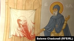 O frescă îl înfățișează pe călugărul georgian Gabriel Urgebadze, dând foc unui steag cu Vladimir Lenin.