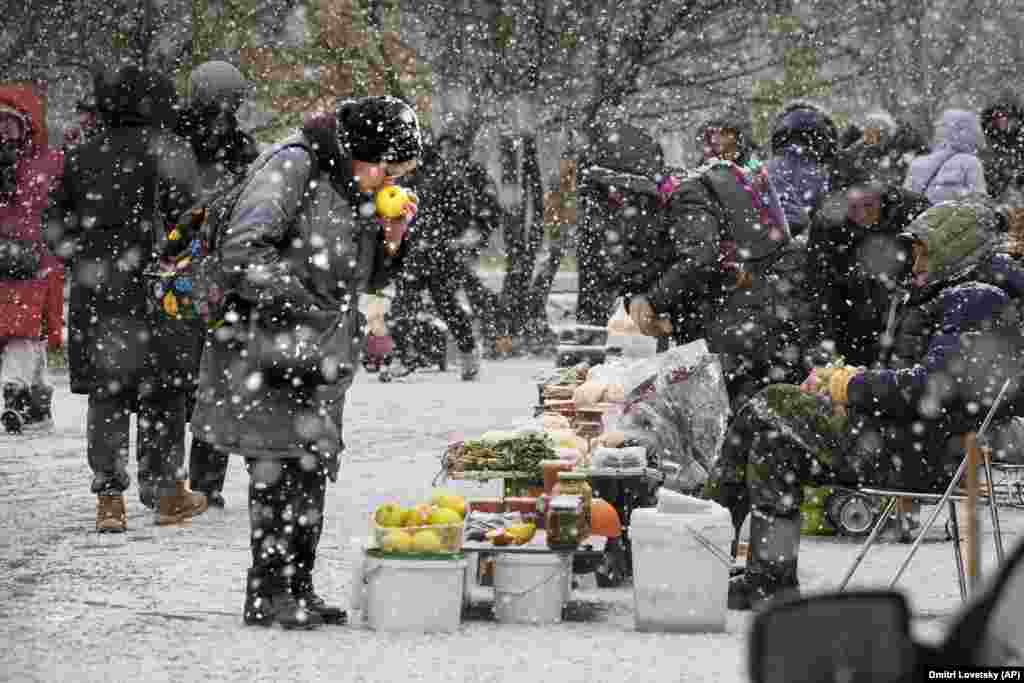 A woman chooses apples from a street vendor in snowfall in St. Petersburg, Russia.