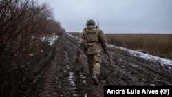 A Ukrainian soldier moves at a position along a tree line on a muddy field.