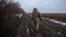 A Ukrainian soldier moves at a position along a tree line on a muddy field.