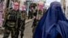 Taliban security personnel stand guard as a burqa-clad Afghan woman walks along a street in the Baharak district of northeastern Badakhshan Province in February.