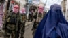 Taliban fighters stand guard as an Afghan woman walks through a market in the Baharak district of Badakhshan Province in February.