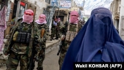 Taliban fighters stand guard as an Afghan woman walks through a market in the Baharak district of Badakhshan Province in February.