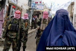 Taliban fighters stand guard as an Afghan woman in a burqa walks on a street in the northern province of Badakhshan in February.