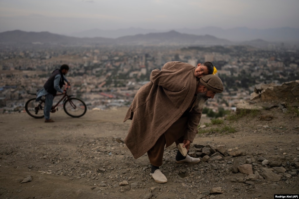 Një burrë që mban mbi kurriz djalin e tij, heq gurët nga një rrugë në Kabul në mënyrë që biçikletat dhe makinat të mund të udhëtojnë më lehtë.